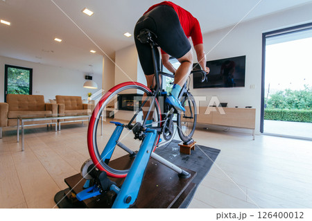 A triathlete riding a triathlon bike on a machine simulation in a modern living room 126400012