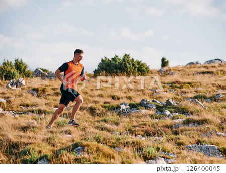 Determined Athlete Running Through Rugged Mountain Terrain at Sunrise. 126400045