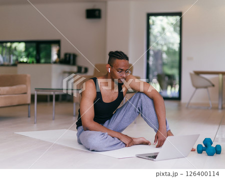 Training At Home. Sporty man doing the training while watching an online tutorial on a laptop, exercising in the living room, free space. 126400114