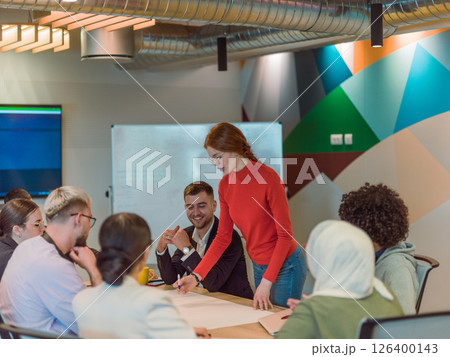A diverse team of business experts in a modern glass office, attentively listening to a colleague's presentation, fostering collaboration and innovation A diverse team of business experts in a modern glass office, attentively listening to a colleague's presentation, fostering collaboration and innovation 126400143