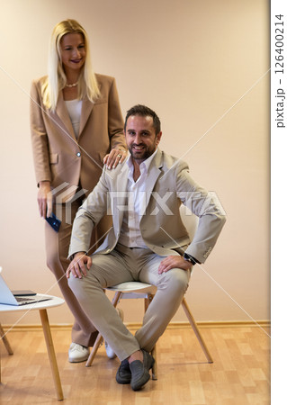 A business couple posing for a photograph together against a beige backdrop, capturing their professional partnership and creating a timeless image of unity and success. A business couple posing for a photograph together against a beige backdrop, capturing their professional partnership and creating a timeless image of unity and success. 126400214