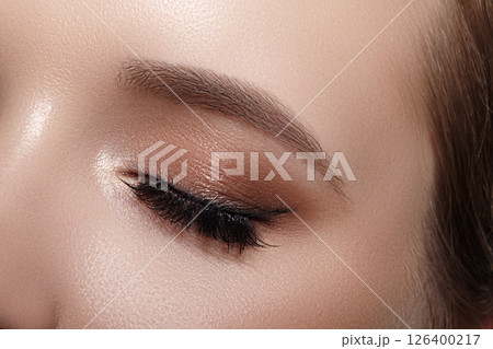 Elegance close-up of female eye with classic dark brown smoky make-up. Macro shot of woman's face part. Beauty, cosmetics and makeup. 126400217