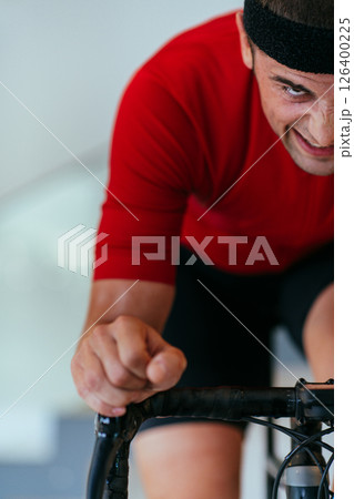 A triathlete riding a triathlon bike on a machine simulation in a modern living room. Training during pandemic conditions. 126400225