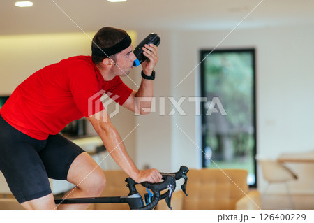 A triathlete riding a triathlon bike on a machine simulation in a modern living room. Training during pandemic conditions. A triathlete riding a triathlon bike on a machine simulation in a modern living room. Training during pandemic conditions. 126400229
