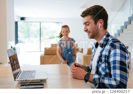 A freelancer sitting at a table in a modern living room, with headphones using a laptop for business video chat, conversation with friends and entertainment 126400257