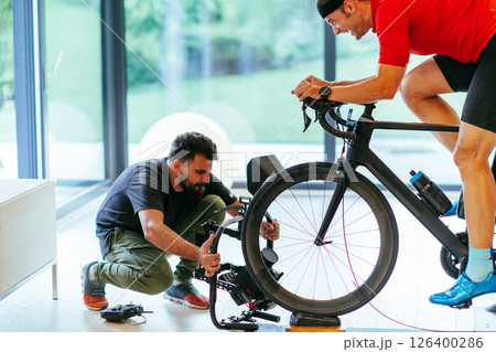 A cameraman filming an athlete riding a triathlon bike on a simulation machine in a modern living room. Training in pandemic conditions 126400286