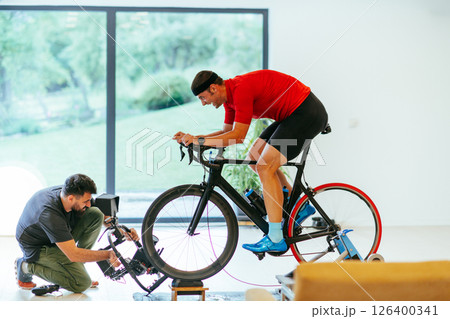 A cameraman filming an athlete riding a triathlon bike on a simulation machine in a modern living room. Training in pandemic conditions 126400341