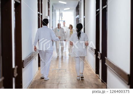 A group of healthcare professionals in white uniforms walking through a hospital hallway while reviewing patient documents and discussing treatment plans. 126400375