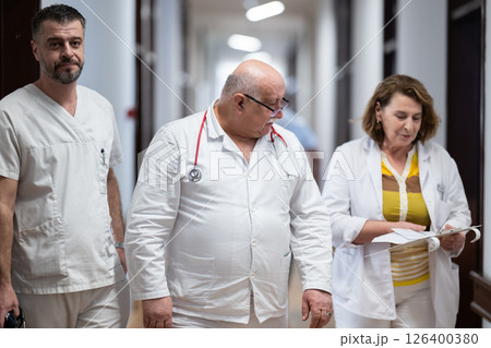 A group of healthcare professionals in white uniforms walking through a hospital hallway while reviewing patient documents and discussing treatment plans. 126400380