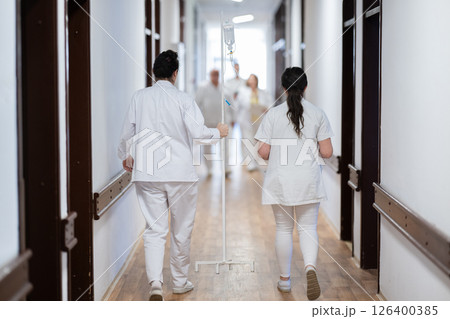 A group of healthcare professionals in white uniforms walking through a hospital hallway while reviewing patient documents and discussing treatment plans. A group of healthcare professionals in white uniforms walking through a hospital hallway while reviewing patient documents and discussing treatment plans. 126400385