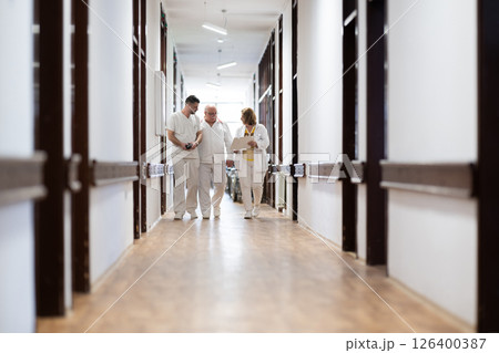 A group of healthcare professionals in white uniforms walking through a hospital hallway while reviewing patient documents and discussing treatment plans. A group of healthcare professionals in white uniforms walking through a hospital hallway while reviewing patient documents and discussing treatment plans. 126400387