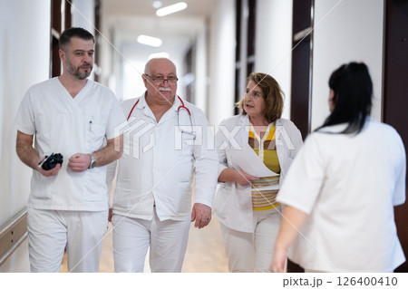 A group of healthcare professionals in white uniforms walking through a hospital hallway while reviewing patient documents and discussing treatment plans. A group of healthcare professionals in white uniforms walking through a hospital hallway while reviewing patient documents and discussing treatment plans. 126400410