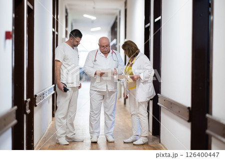 A group of healthcare professionals in white uniforms walking through a hospital hallway while reviewing patient documents and discussing treatment plans. A group of healthcare professionals in white uniforms walking through a hospital hallway while reviewing patient documents and discussing treatment plans. 126400447