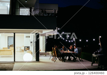 A group of young diverse people having dinner on the terrace of a modern house in the evening. Fun for friends and family. Celebration of holidays, weddings with barbecue 126400460