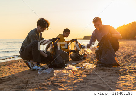 Earth day. Volunteers activists team collects garbage cleaning of beach coastal zone. Woman mans puts plastic trash in garbage bag on ocean shore. Environmental conservation coastal zone cleaning 126401189