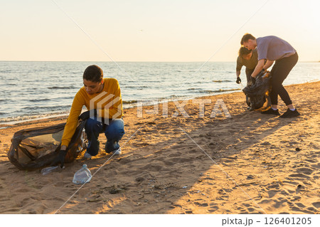 Earth day. Volunteers activists team collects garbage cleaning of beach coastal zone. Woman mans puts plastic trash in garbage bag on ocean shore. Environmental conservation coastal zone cleaning 126401205