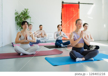 Yoga mindfulness meditation. Group of sporty people doing exercise in studio for class for yoga wellness mindfulness meditation. Men women practicing yoga sitting in lotus pose meditating relaxing Yoga mindfulness meditation. Group of sporty people doing exercise in studio for class for yoga wellness mindfulness meditation. Men women practicing yoga sitting in lotus pose meditating relaxing 126401216