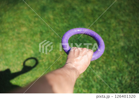 Owner holding a purple ring toy outdoors on green grass, ready to play with their dog 126401320