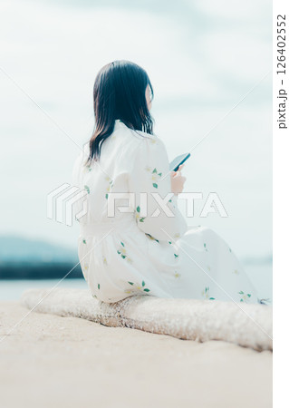 花柄ワンピースの女性が浜辺でスマートフォンを見る姿 花柄ワンピースの女性が浜辺でスマートフォンを見る姿 126402552