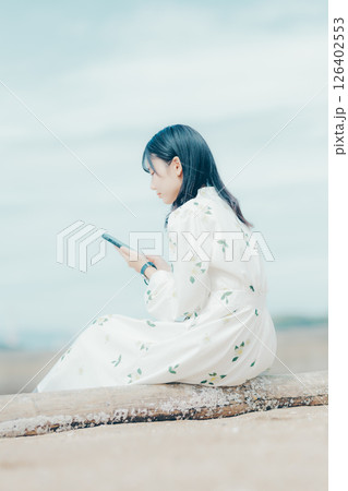 花柄ワンピースの女性が浜辺でスマートフォンを見る姿 花柄ワンピースの女性が浜辺でスマートフォンを見る姿 126402553
