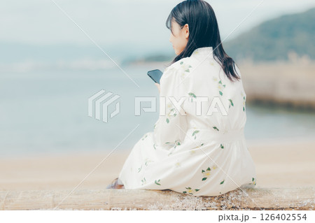 花柄ワンピースの女性が浜辺でスマートフォンを見る姿 126402554