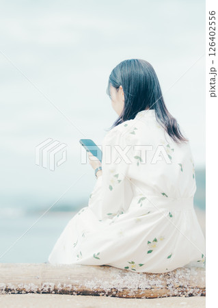 花柄ワンピースの女性が浜辺でスマートフォンを見る姿 花柄ワンピースの女性が浜辺でスマートフォンを見る姿 126402556