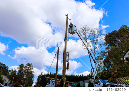 Utility workers use lift trucks to repair power lines while ensuring safety in residential area during works day. Utility workers use lift trucks to repair power lines while ensuring safety in residential area during works day. 126402929