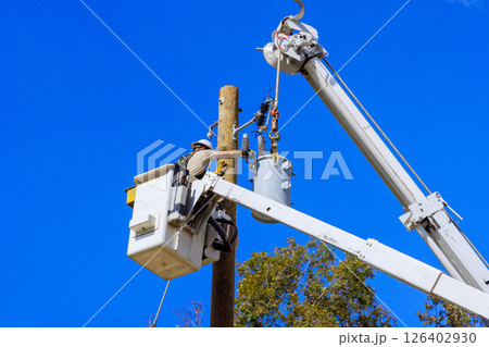 Utility worker is repairing equipment on power lines from lift truck under clear blue sky. 126402930