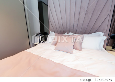 A cozy modern hotel bed with pastel pillows, elegant headboard and soft white bedding in a relaxing interior 126402975