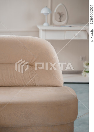 Elegant beige curved sofa in a light-toned interior, featuring a dressing table, decorative elements, and a calm, inviting atmosphere with soft textures 126403204