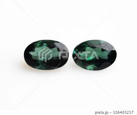 Two oval-cut natural chrome tourmaline gemstones are presented on a white background, showcasing their deep, rich green hue and faceted surfaces, with light reflections creating a sparkling effect Two oval-cut natural chrome tourmaline gemstones are presented on a white background, showcasing their deep, rich green hue and faceted surfaces, with light reflections creating a sparkling effect 126403217