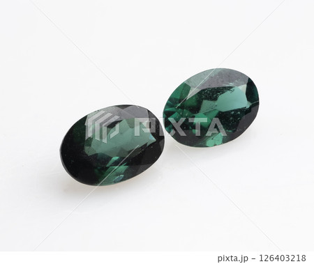Pair of Natural Chrome Tourmaline gemstones, oval-shaped, displaying a deep forest green hue with subtle variations and internal inclusions, resting on a white background 126403218