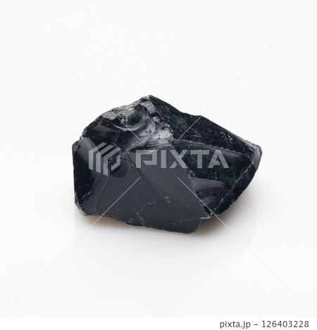 A raw, dark, glossy black obsidian rock fragment with internal flow patterns and subtle grey inclusions, showcasing a vitreous luster and sharp edges, isolated on a bright white background A raw, dark, glossy black obsidian rock fragment with internal flow patterns and subtle grey inclusions, showcasing a vitreous luster and sharp edges, isolated on a bright white background 126403228