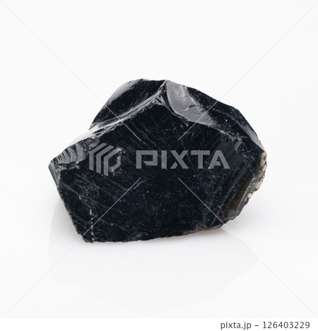 A striking, raw piece of natural black obsidian rock exhibiting a glossy, glass-like surface, sharp edges, and a fractured texture, its dark hue reflecting light, showcasing volcanic origin 126403229