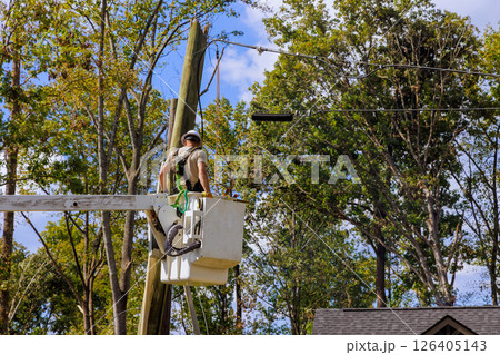 Utility worker stands in bucket lift fixing electrical lines above neighborhood with after hurricane Utility worker stands in bucket lift fixing electrical lines above neighborhood with after hurricane 126405143