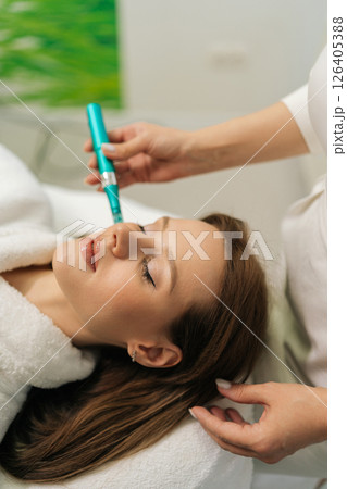 Vertical shot of professional beautician performing microneedling treatment with dermapen on female patient forehead, targeting skin rejuvenation enhancing collagen production, close-up, slow motion 126405388