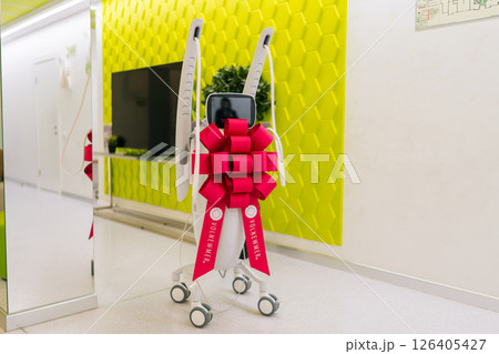 Modern mesotherapy machine with festive bow in corridor of new beauty clinic or medical center, symbolizing innovation in skincare, aesthetic medicine, nobody. Concept of beauty treatment. Modern mesotherapy machine with festive bow in corridor of new beauty clinic or medical center, symbolizing innovation in skincare, aesthetic medicine, nobody. Concept of beauty treatment. 126405427