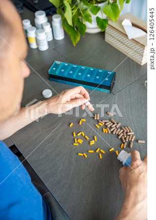 Man sorting his pills and supplements into a weekly pill organizer. Concept of medication management and daily health routine 126405445