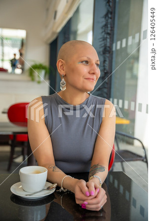Confident young woman with cancer enjoying coffee in a cafe, embracing life despite illness. The concept shows that a cancer diagnosis does not take away the ability to enjoy normal activities Confident young woman with cancer enjoying coffee in a cafe, embracing life despite illness. The concept shows that a cancer diagnosis does not take away the ability to enjoy normal activities 126405449