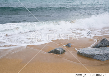 Waves crashing on sandy beach with rocks and clear sky Waves crashing on sandy beach with rocks and clear sky 126406176