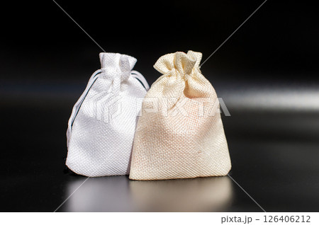 Two cloth bags on black background: white and beige textured fabric pouches 126406212