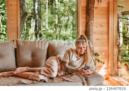 Woman with Smartphone Lying on Sofa in Log Cabin 126407628