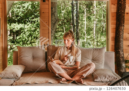 Woman Relaxing in Log Cabin with Coffee and Book 126407630