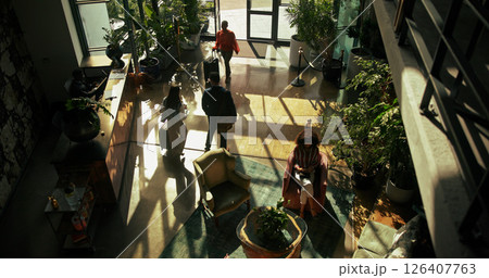 Above, business trip and people in lobby of hotel for checkin, arrival or reception desk. Hospitality, men and women at entrance of travel accommodation with luggage, service or walking with suitcase 126407763