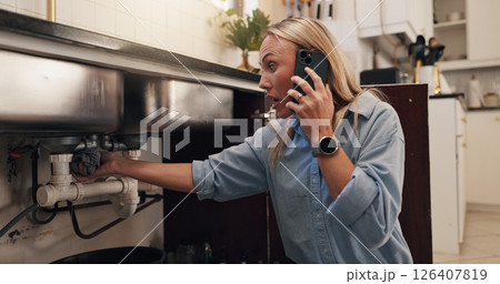 Woman, phone call and stress by kitchen sink for leak, emergency and talk with shock at apartment. Person, smartphone and contact for repair, help and plumbing services for drain in morning at house 126407819