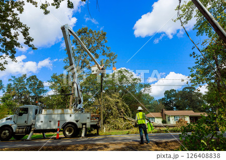 Workers operate bucket truck to repairs power lines in suburban neighborhood after storm. Workers operate bucket truck to repairs power lines in suburban neighborhood after storm. 126408838