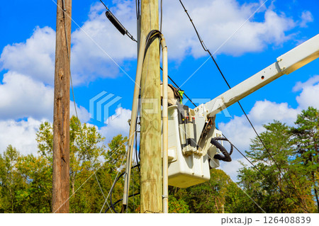 Workers use crane truck from bucket lift to conduct maintenance on power lines against backdrop after hurricane Workers use crane truck from bucket lift to conduct maintenance on power lines against backdrop after hurricane 126408839