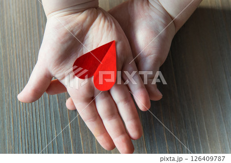 Red paper handmade hearts in child hands on the wood background. Sign of love. A gift for Valentines Day and Mothers Day. Red paper handmade hearts in child hands on the wood background. Sign of love. A gift for Valentines Day and Mothers Day. 126409787
