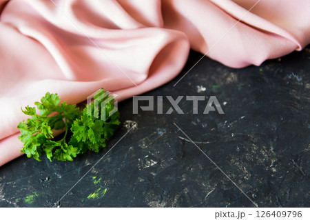 Pink gentle silk fabric and green spring herbs on the rough black texture background. Pink gentle silk fabric and green spring herbs on the rough black texture background. 126409796