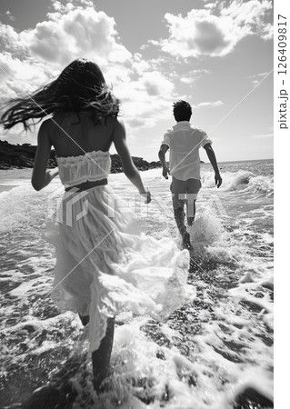 Romantic beach scene with man and woman running into the sea, captured in black and white 126409817